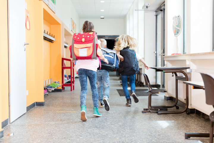 Kinder, die mit Rucksäcken aus der Schule laufen.